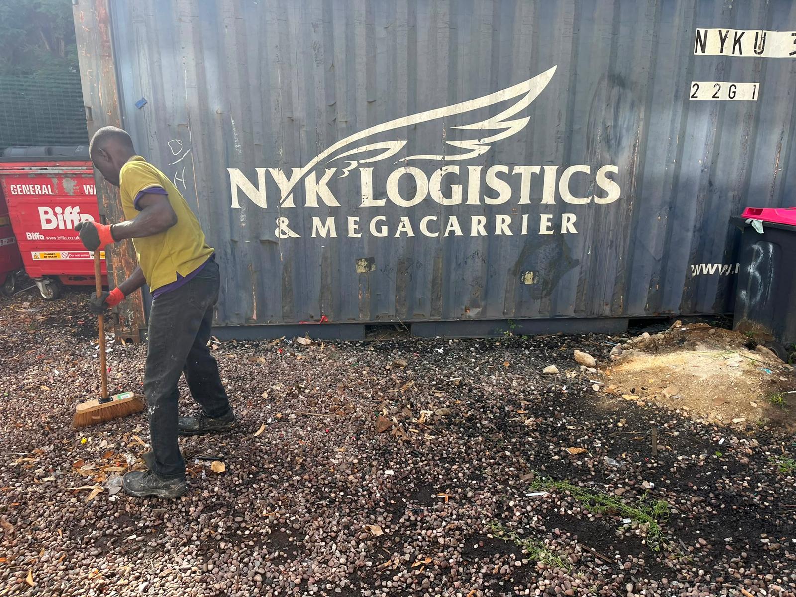 After: the same commercial site cleared and swept, with a worker finishing the tidy-up next to the container.